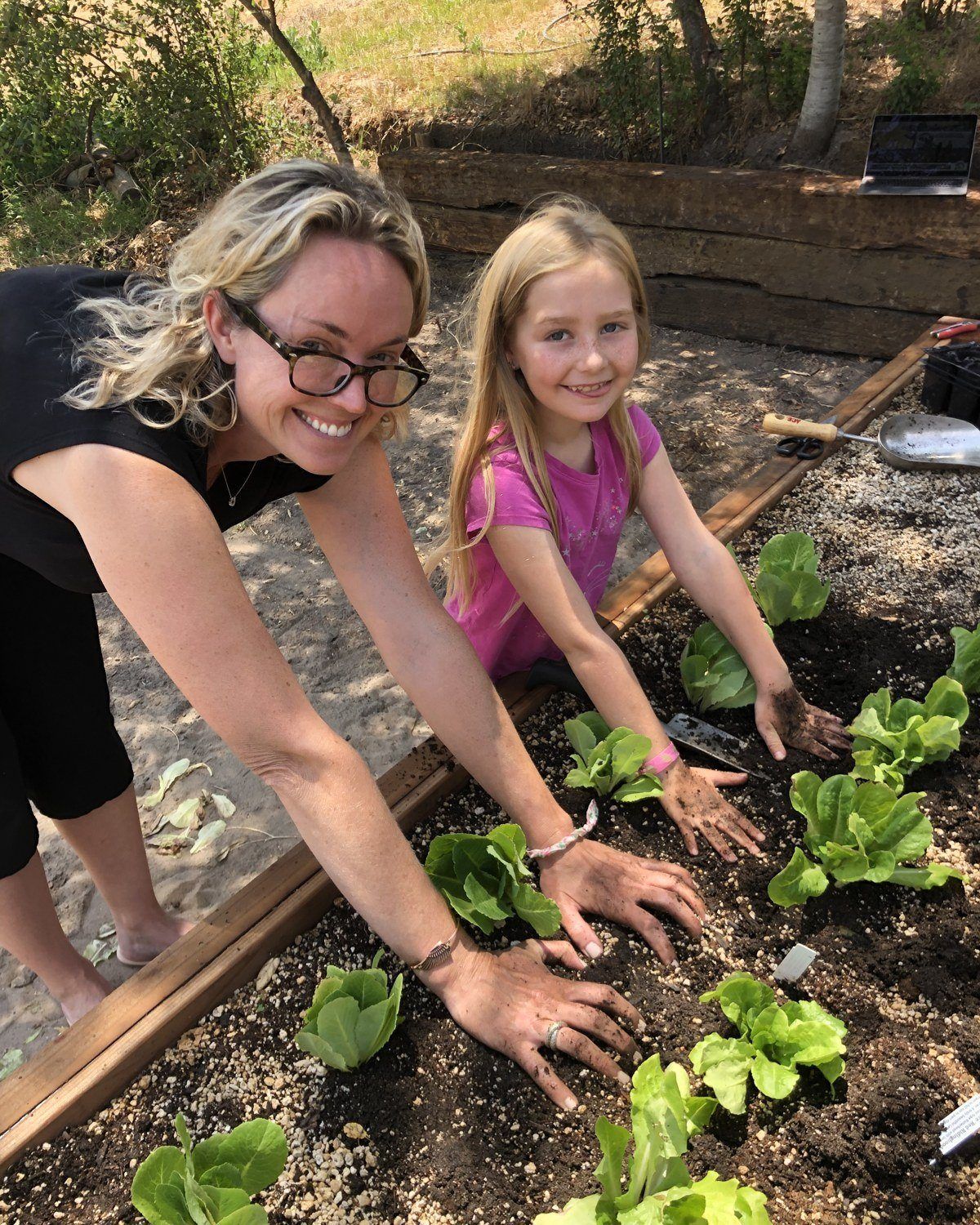A mother and daughter planting seedlings with dirt-covered hands